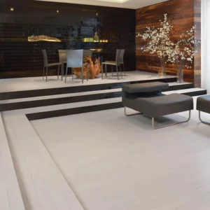 Modern dining and seating area with Red Oak Nordic flooring from Admiration Collection, featuring a raised platform design, sleek black and white furniture, and decorative wood-paneled walls