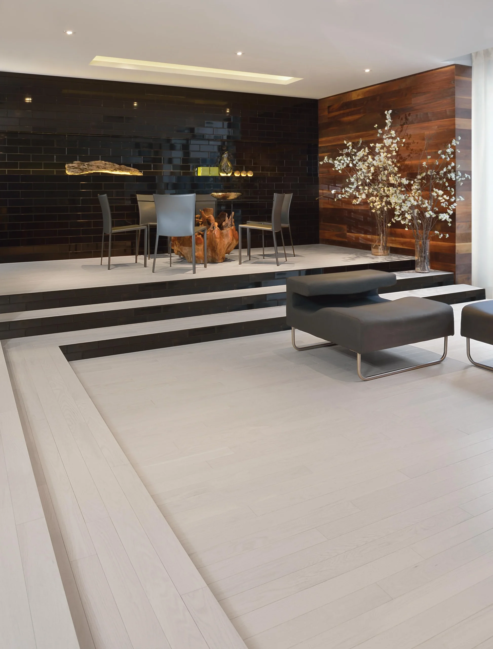 Modern dining and seating area with Red Oak Nordic flooring from Admiration Collection, featuring a raised platform design, sleek black and white furniture, and decorative wood-paneled walls